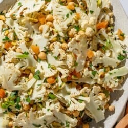 An overhead photo of a shaved cauliflower salad in a serving bowl next to a wooden serving fork.