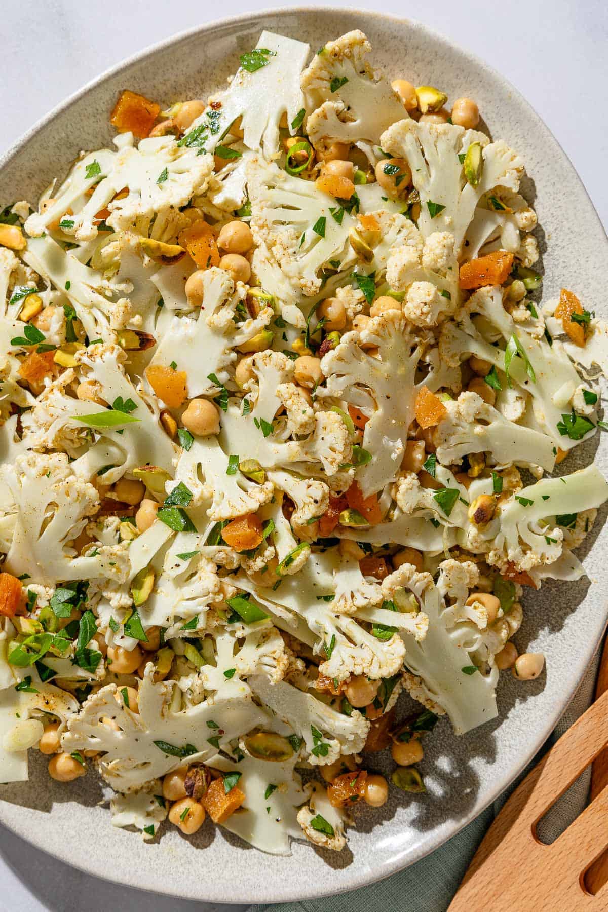 An overhead photo of a shaved cauliflower salad in a serving bowl next to a wooden serving fork.
