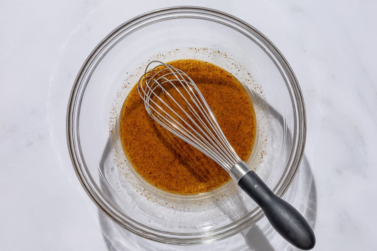 The dressing for the shaved cauliflower salad in a bowl with a whisk.