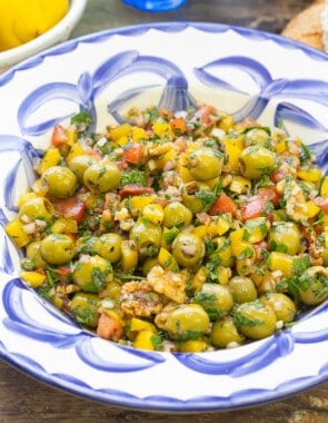 A close up of olive salad in a serving bowl. Next to this is a bowl of lemons, some crusty bread and three forks.