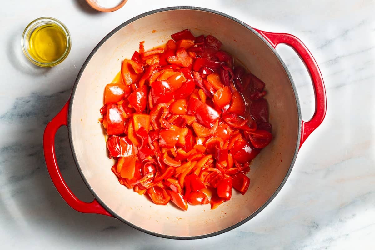 Chopped peppers cooking in a pot. Next to this are bowls are olive oil and salt.