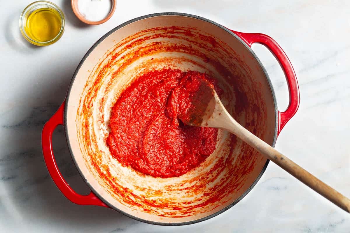 The red pepper paste in a large pot with a wooden spoon. Next to this are bowls of olive oil and salt.