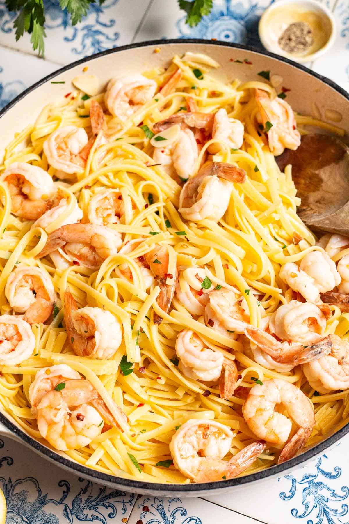 A close up of shrimp linguine in a serving bowl with a wooden spoon.