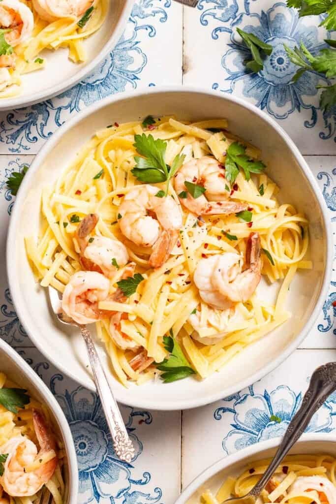 An overhead photo of shrimp linguine in a bowl with a fork .