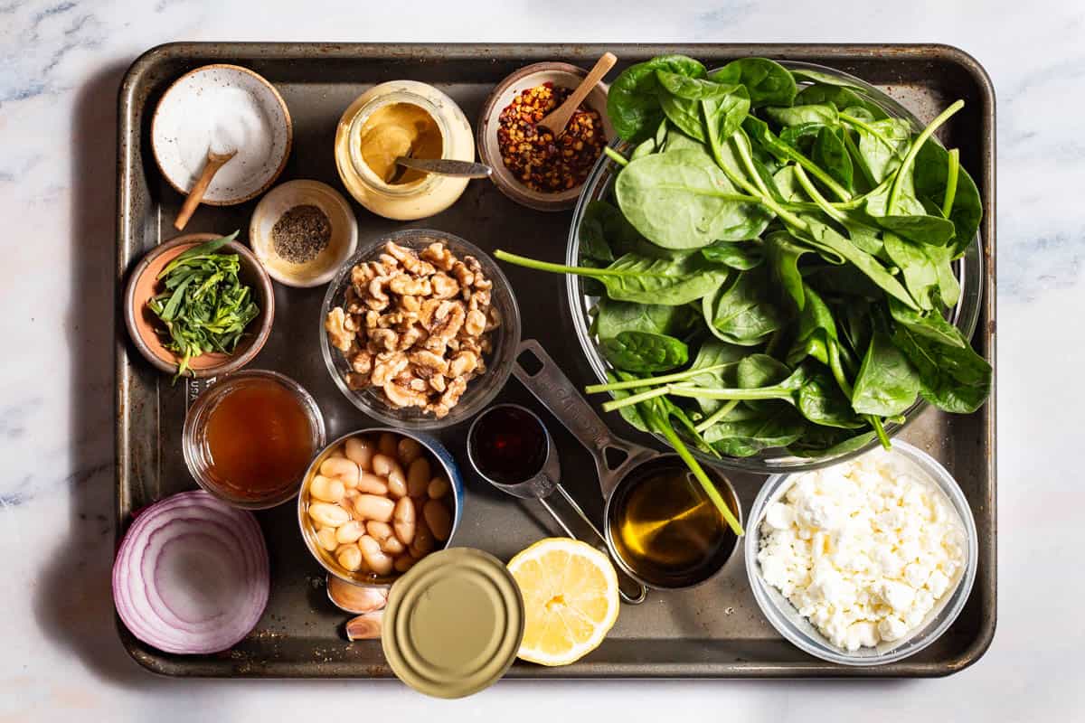 Ingredients for wilted spinach salad including spinach, red onion, apple cider vinegar, honey, tarragon, walnuts, dijon, red pepper flakes, pepper, olive oil, garlic, cannellini beans, lemon and goat cheese.