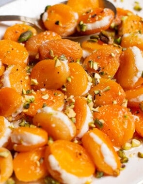 Stuffed apricots topped with pistachios on a serving platter with a spoon.