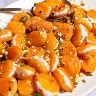 Stuffed apricots topped with pistachios on a serving platter with a spoon.