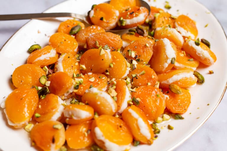 Stuffed apricots topped with pistachios on a serving platter with a spoon.