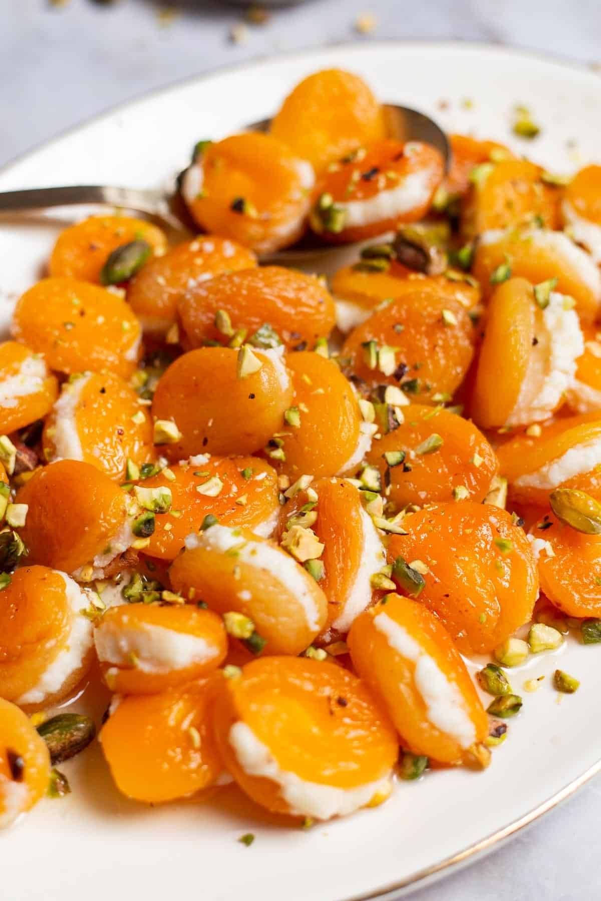 A close up of stuffed apricots topped with pistachios on a serving platter with a spoon.