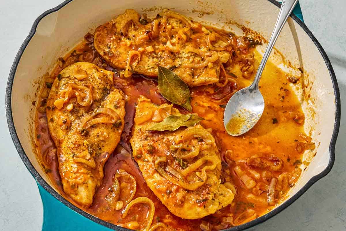 A close up of braised chicken breasts in a skillet with a spoon.