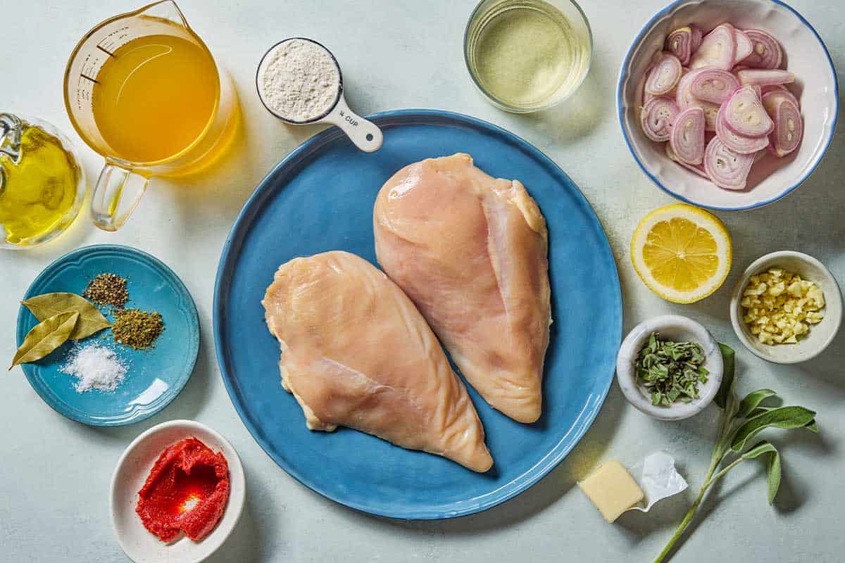 Ingredients for braised chicken breast including chicken breasts, shallots, pepper, oregano, flour, olive oil, butter, garlic, sage, tomato paste, bay leaves, white wine, chicken stock and a lemon.