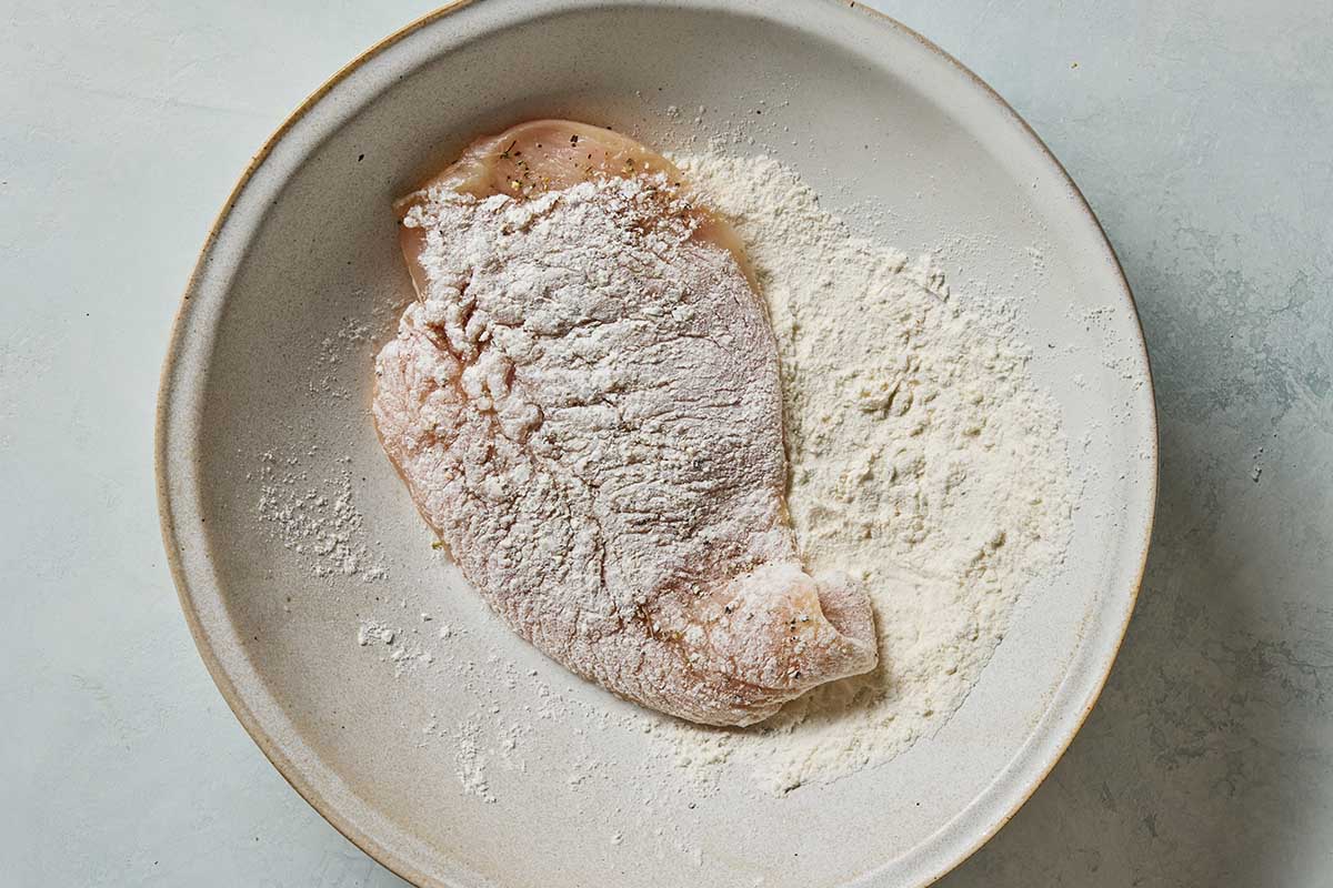 A chicken breast coated in flour on a plate.