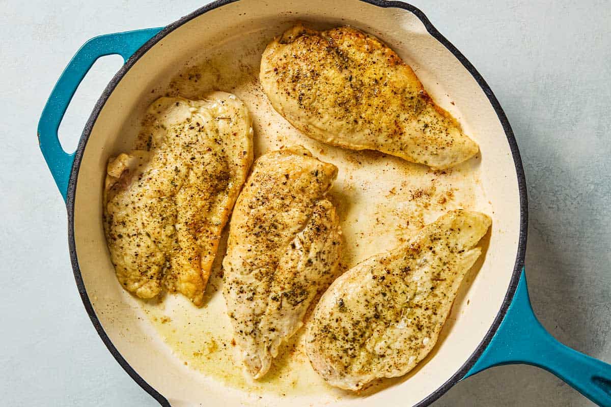 4 chicken breasts being braised in a skillet.