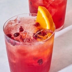 A close up of 2 pomegranate fizz mocktails garnished with pomegranate seeds and orange wedges.