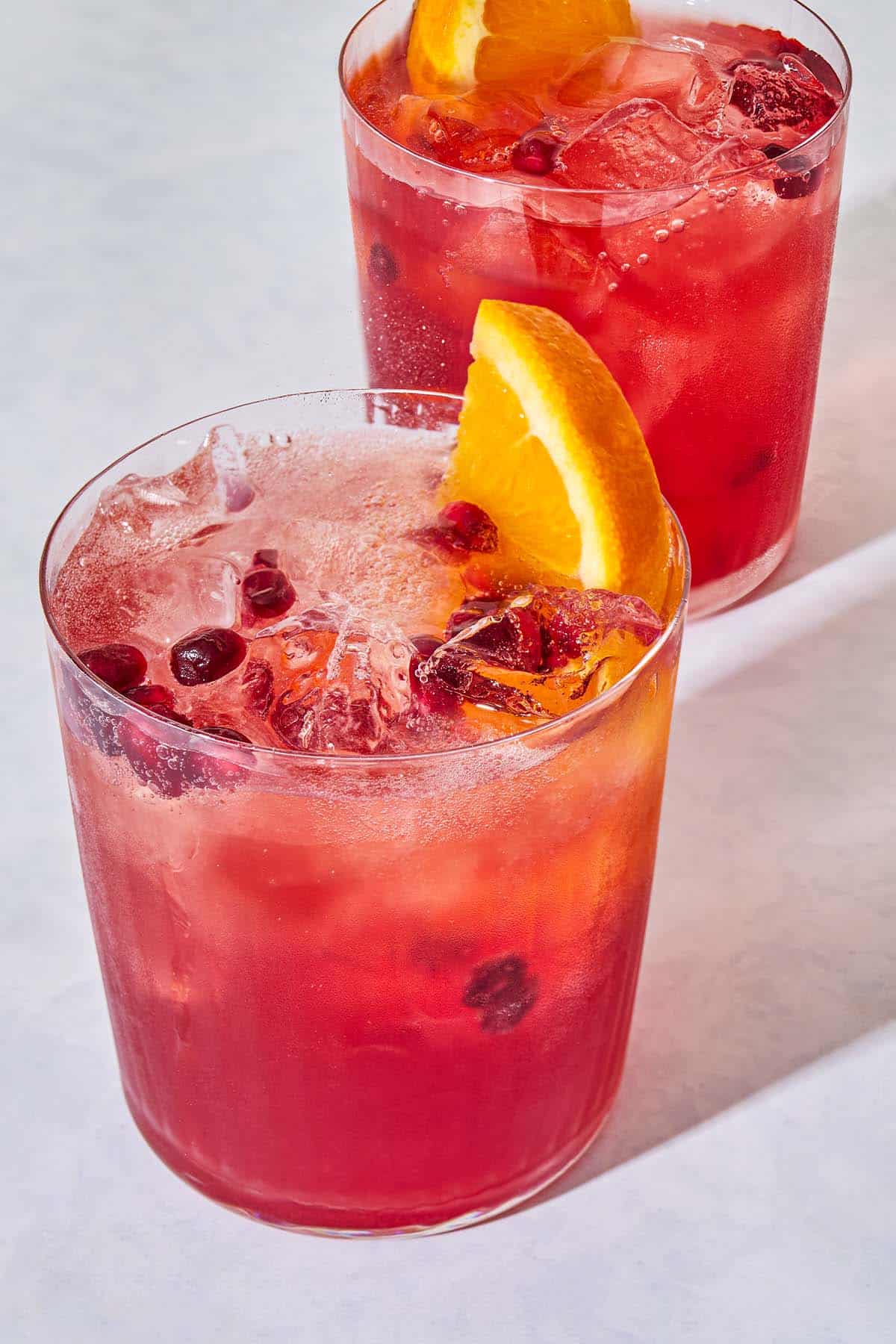 A close up of 2 pomegranate fizz mocktails garnished with pomegranate seeds and orange wedges.