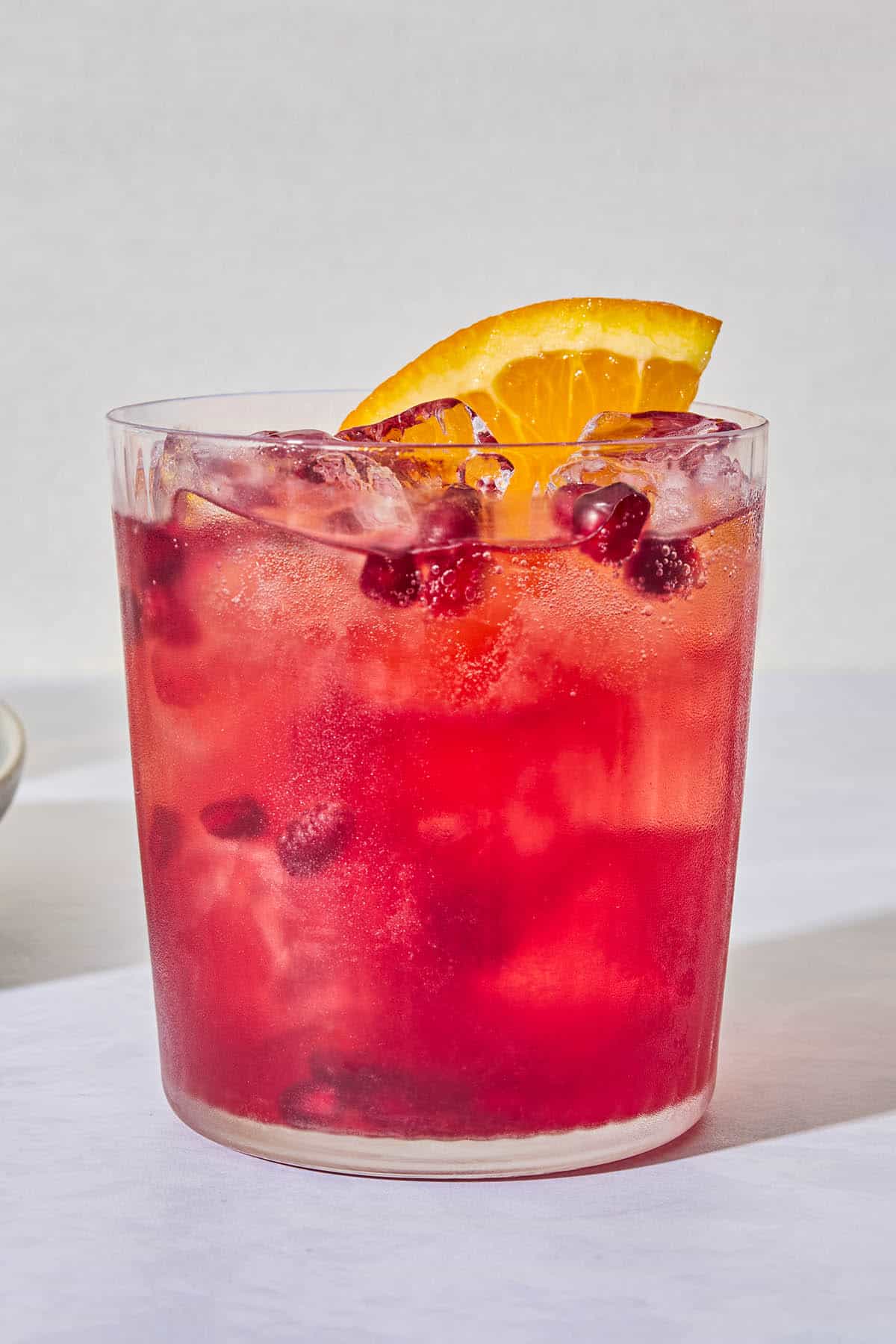 A close up of a pomegranate fizz mocktail garnished with pomegranate seeds and an orange wedge.