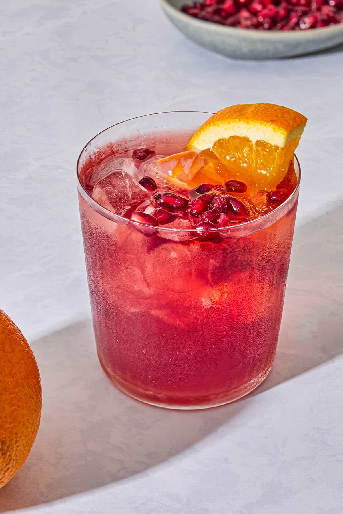 A pomegranate fizz mocktail garnished with pomegranate seeds and an orange wedge.