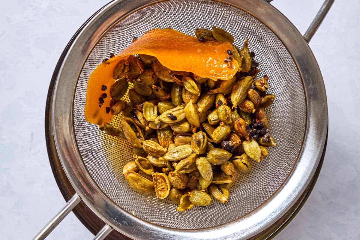 The cardamom pods and orange zest in a strainer.