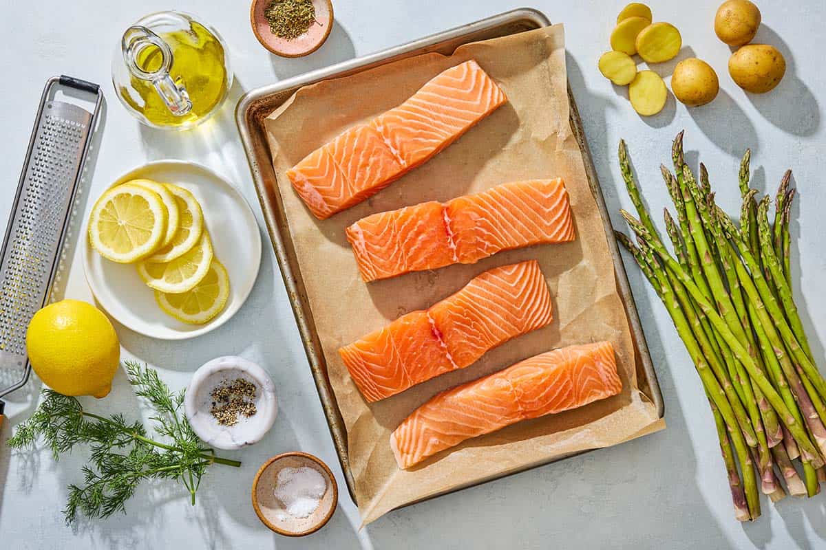 Ingredients for salmon en papillote including salmon, oregano, lemon, salt, pepper, olive oil, baby potatoes, asparagus and dill.