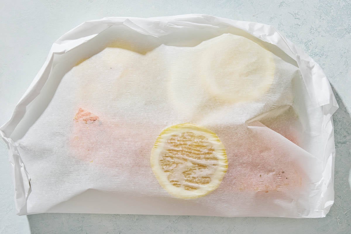 The unbaked salmon, lemon and vegetables completely wrapped in parchment paper.