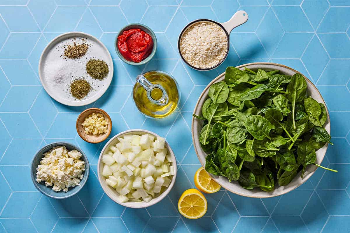 Ingredients for spanakorizo including rice, olive oil, onion, baby spinach, lemon, garlic tomato paste, dried mint, dried dill, salt, pepper and feta cheese.