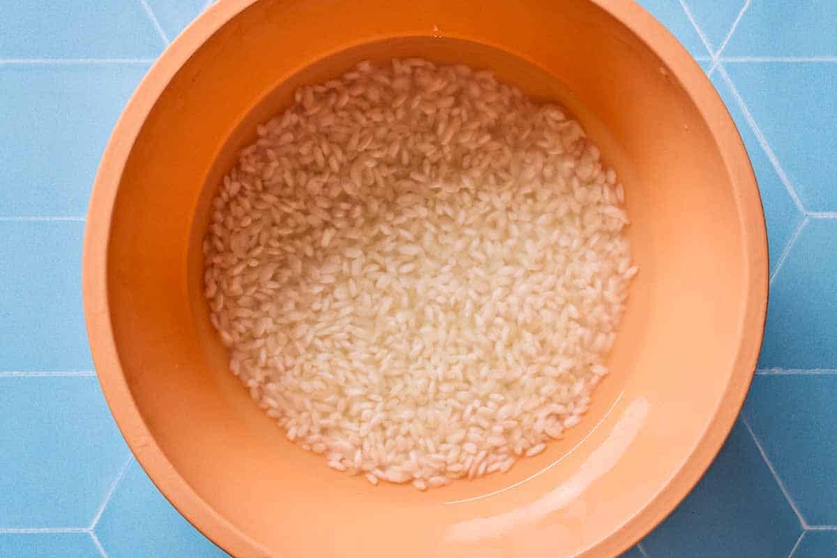 An overhead photo of rice soaking in a bowl of water for spinach rice recipe.