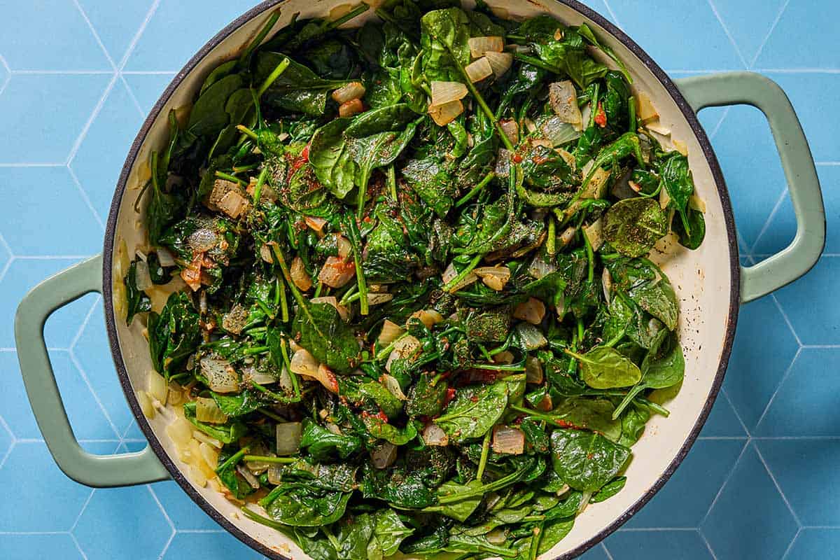 An overhead photo of onions and spinach after being sauteed in a skillet.