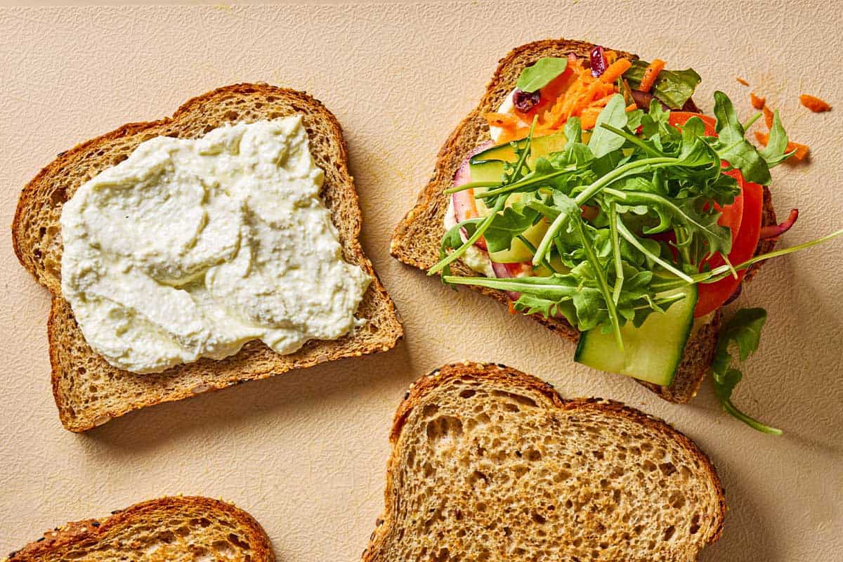 An overhead photo of 4 pieces of toast, one with whipped feta, one with Greek-style slaw, and two that are plain.