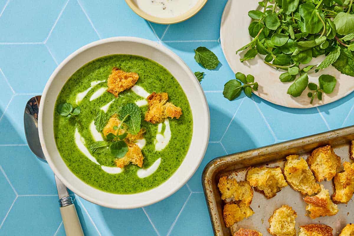 One bowl of watercress soup with four croutons on top and more croutons on the side.