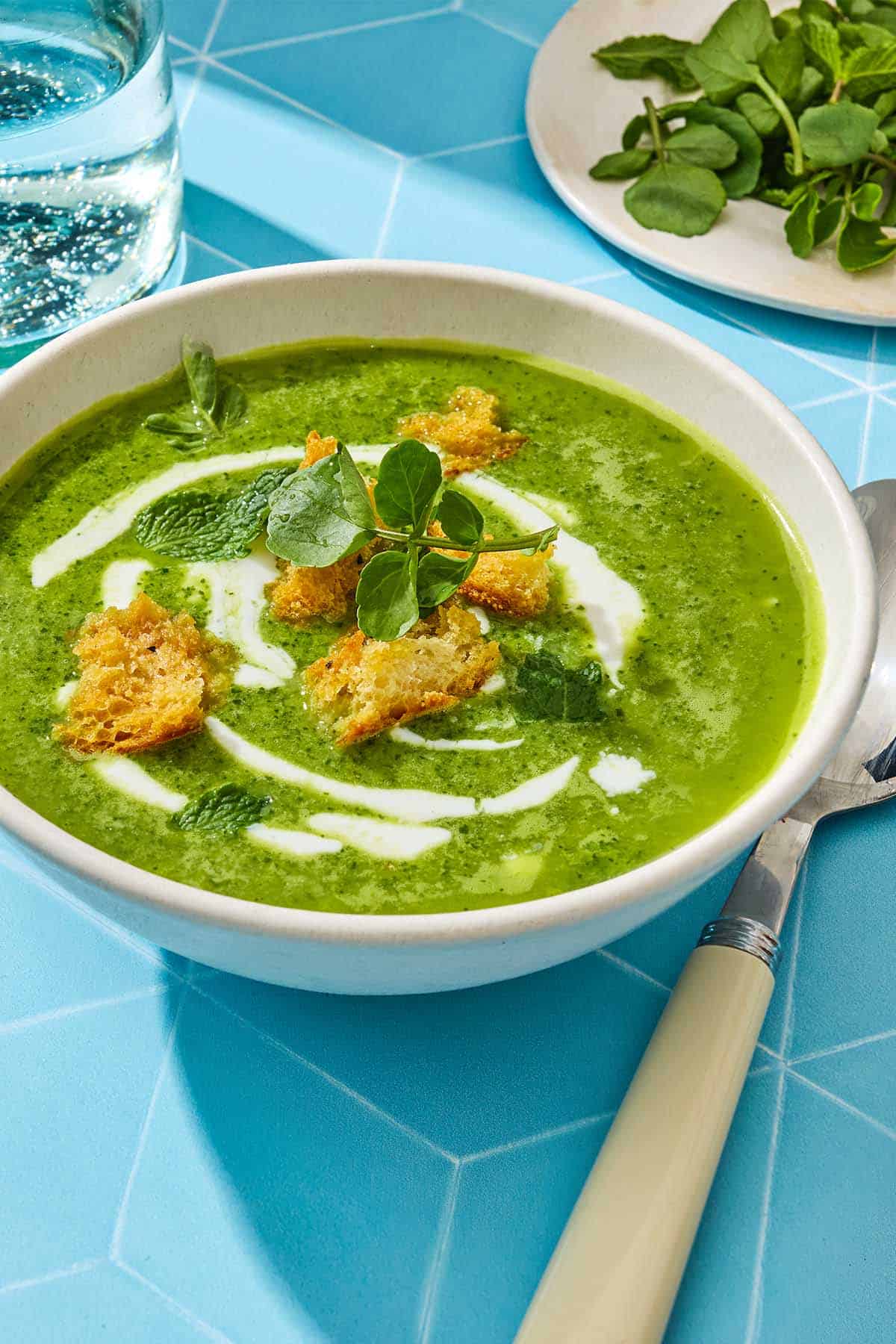 Side shot of a bowl of watercress soup with croutons, mint and a drizzle of Greek yogurt on top.