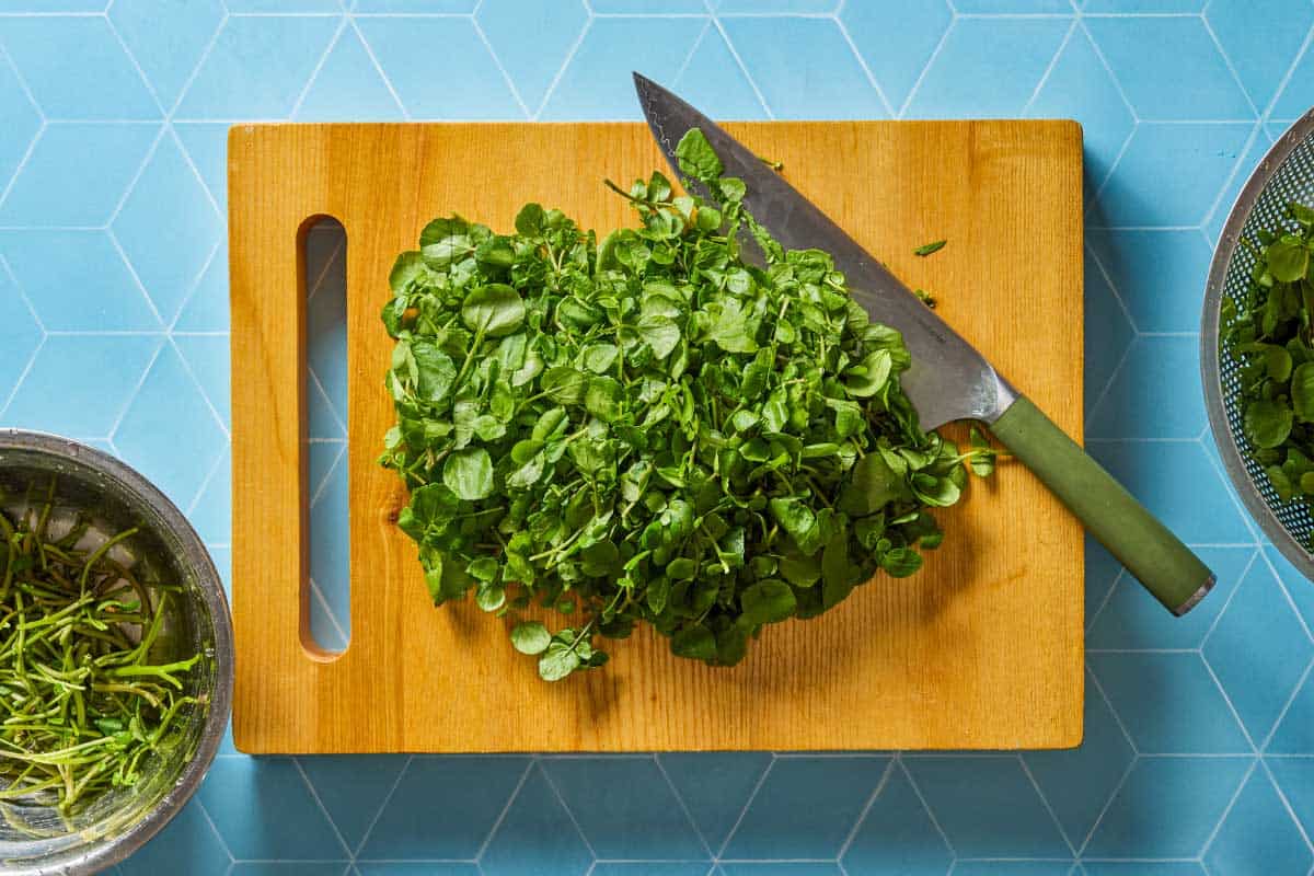 watercress on a cutting board with a knife.