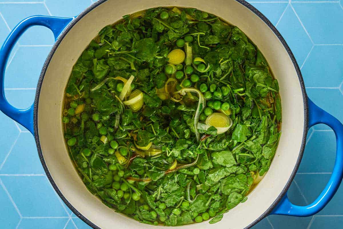 Watercress soup simmering in a blue pot. You can see the watercress, leeks, and peas.