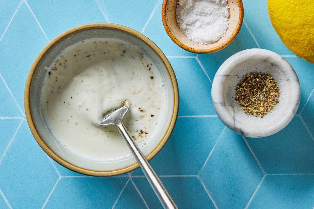Yogurt sauce in a bowl with salt and pepper on the side.