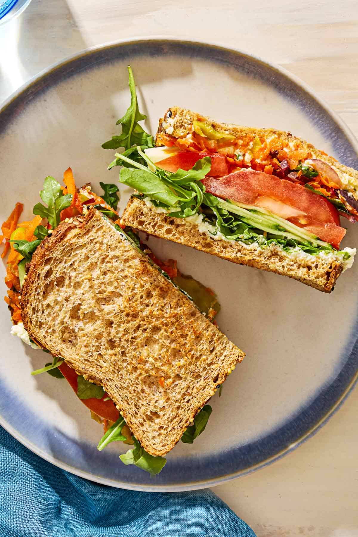 A veggie sandwich cut in half on a plate next to a cloth napkin.
