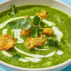 Close up of watercress soup with croutons, mint, and a sprig of watercress on top.
