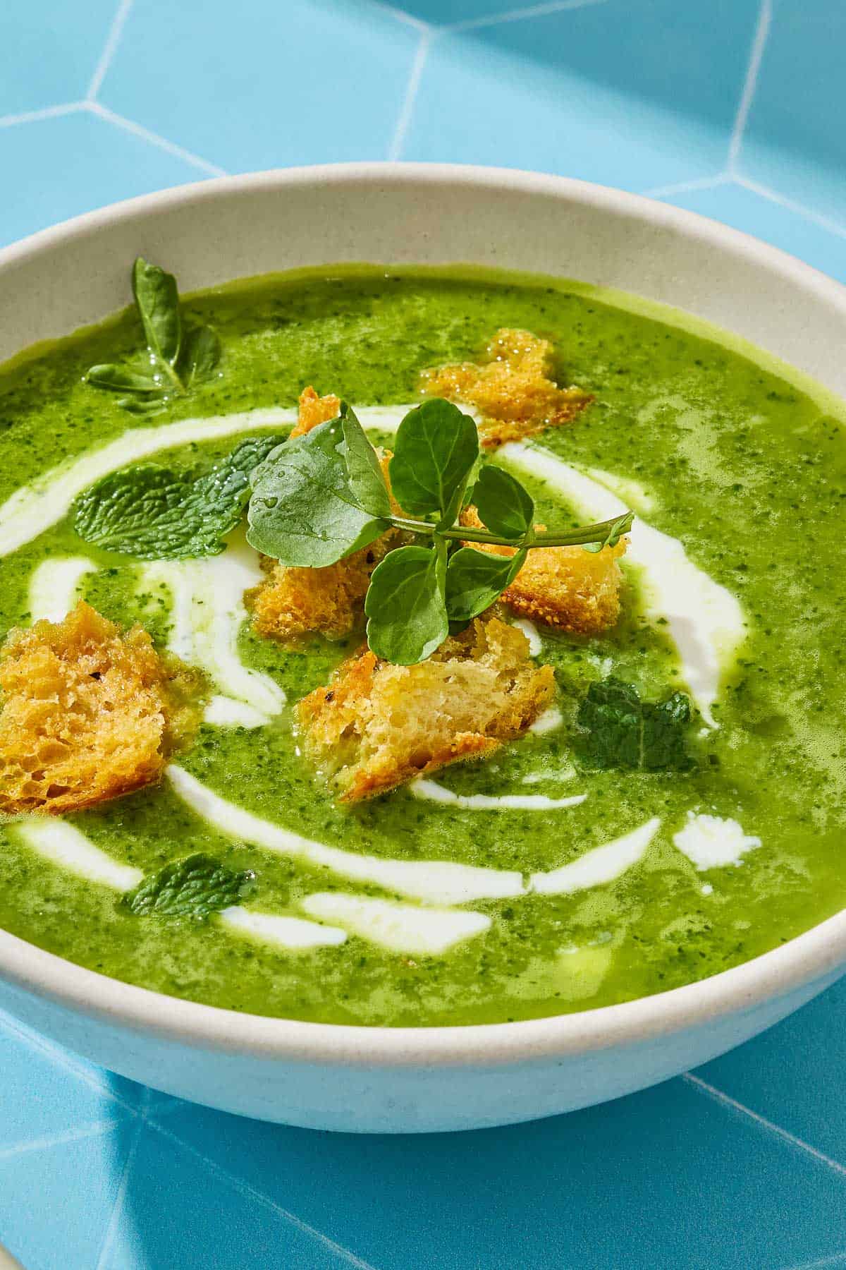 Close up of watercress soup with croutons, mint, and a sprig of watercress on top.
