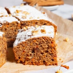 A close up of a slice of the healthy carrot cake in front of the rest of the cake on a sheet of parchment paper.