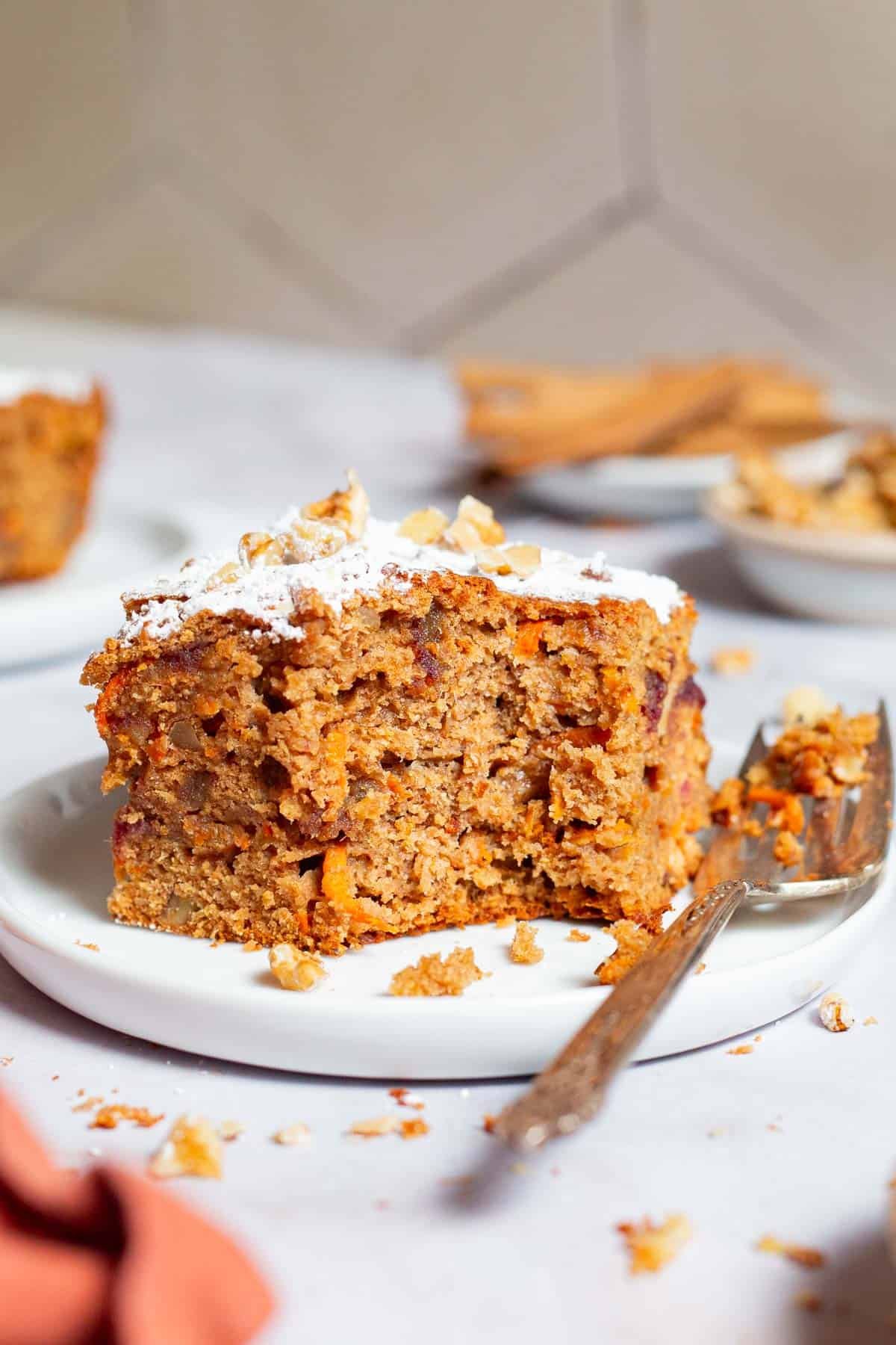 A close up of a slice of healthy carrot cake with a bite taken out of it on a plate with a fork.