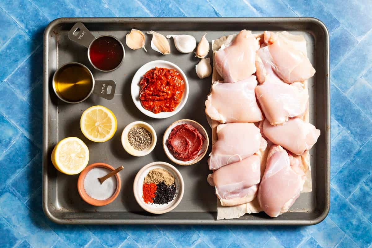 Ingredients for harissa honey chicken, including chicken thighs, salt, pepper, garlic, paprika, coriander, urfa biber, olive oil, lemon, honey, tomato paste, and harissa.