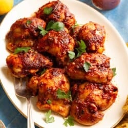 Side shot of a platter with 8 honey harissa chicken thighs and a sprinkling of fresh parsley.