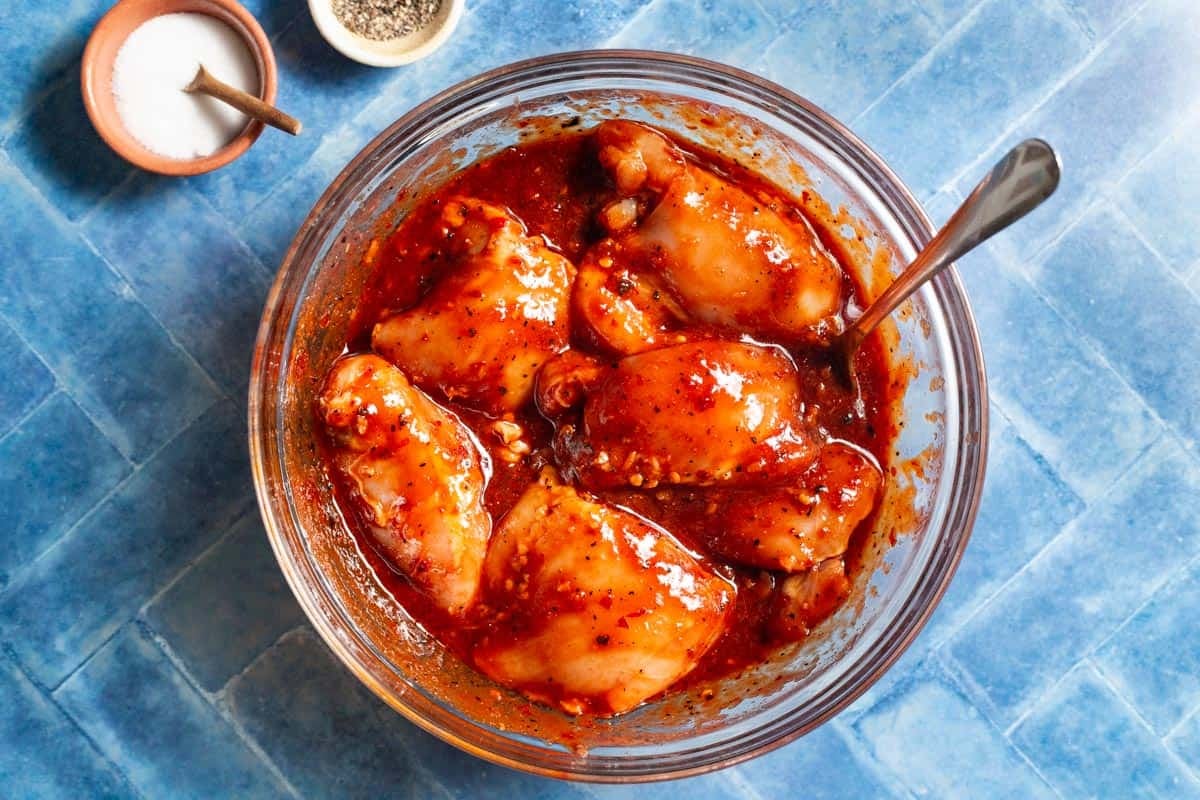Chicken thighs in a glass bowl that have been fully coated in honey harissa marinade.