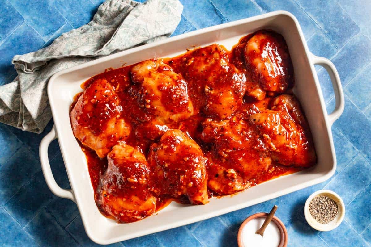 chicken thighs with honey harissa marinade in a rectangular baking dish.