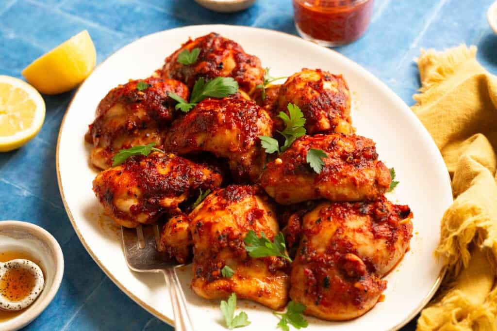 honey harissa chicken on a platter with parsley leaves on top.