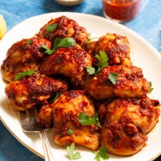 honey harissa chicken on a platter with parsley leaves on top.