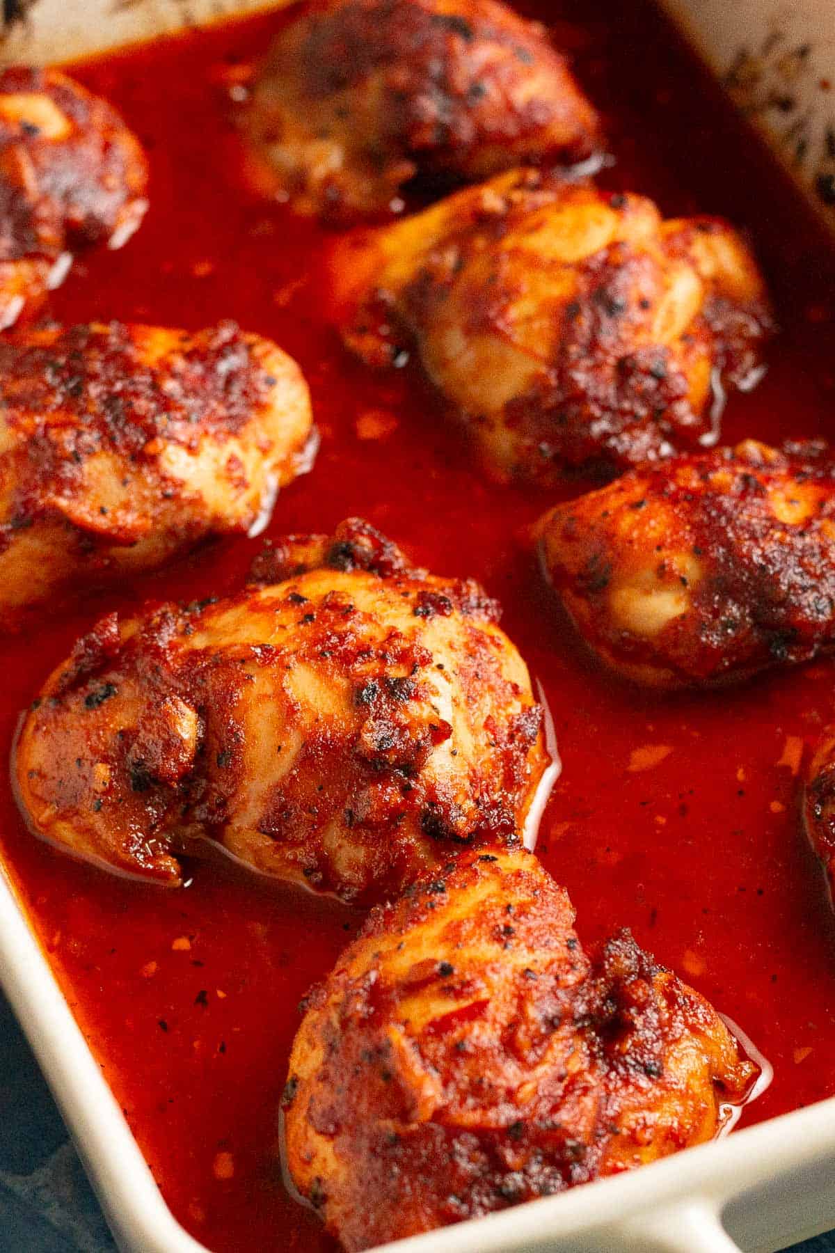 Close up shot of oven baked chicken thighs in a bright red harissa honey sauce.
