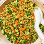 An overhead close up of herby freekeh salad in a serving bowl with serving utensils.