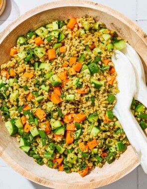 An overhead close up of herby freekeh salad in a serving bowl with serving utensils.