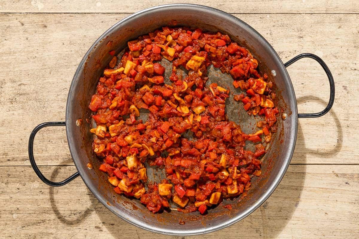 Seasoned chopped onions, red bell pepper, garlic tomatoes and squid being sauteed in a skillet.
