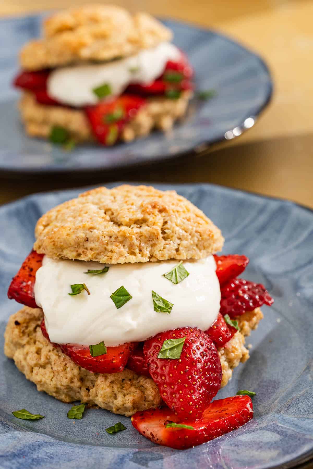 A close up of a strawberry shortcake on a plate in front of another shortcake on a plate.
