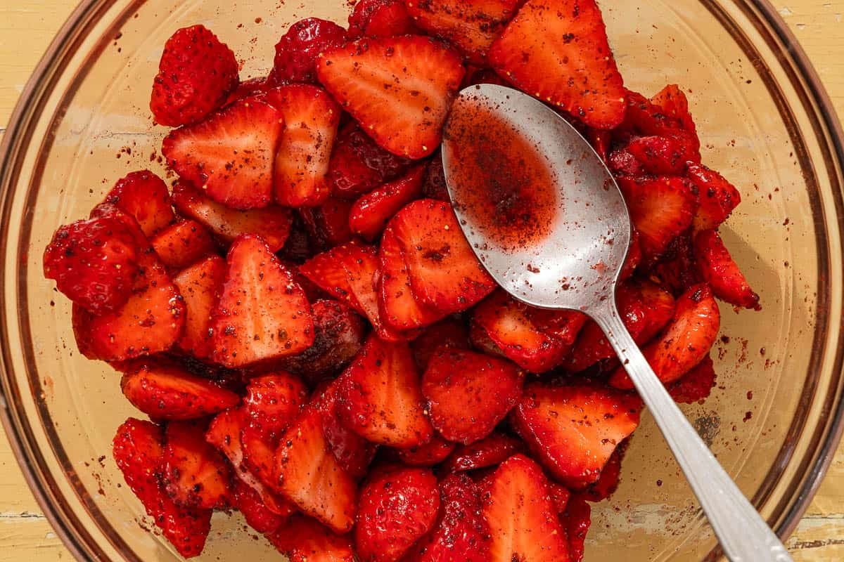 A strawberries tossed with citrus juice, sumac and sugar in a bowl with a spoon.